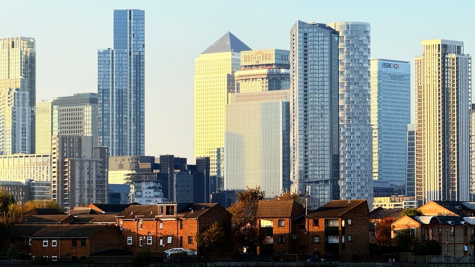 A cityscape featuring modern office buildings with reflective glass facades, including a prominent tall blue-tinted skyscraper on the left and a variety of other high-rise structures with different ar